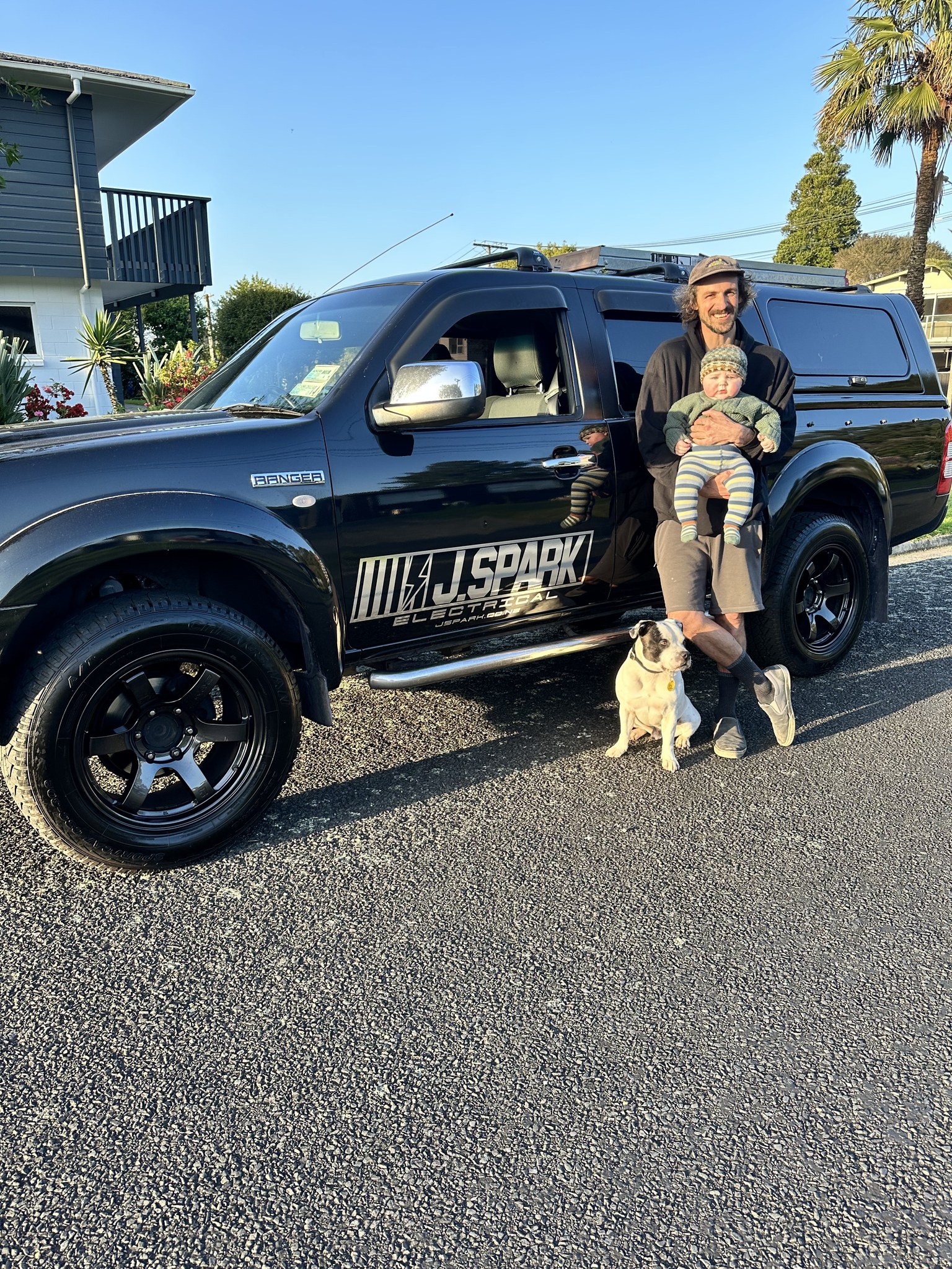 Jono holding his son, with their dog, beside the J Spark Electrical ute